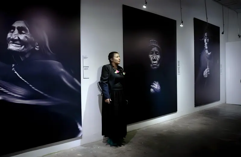 Una mujer de negro en una galería, entre grandes retratos en blanco y negro de abuelas andinas.