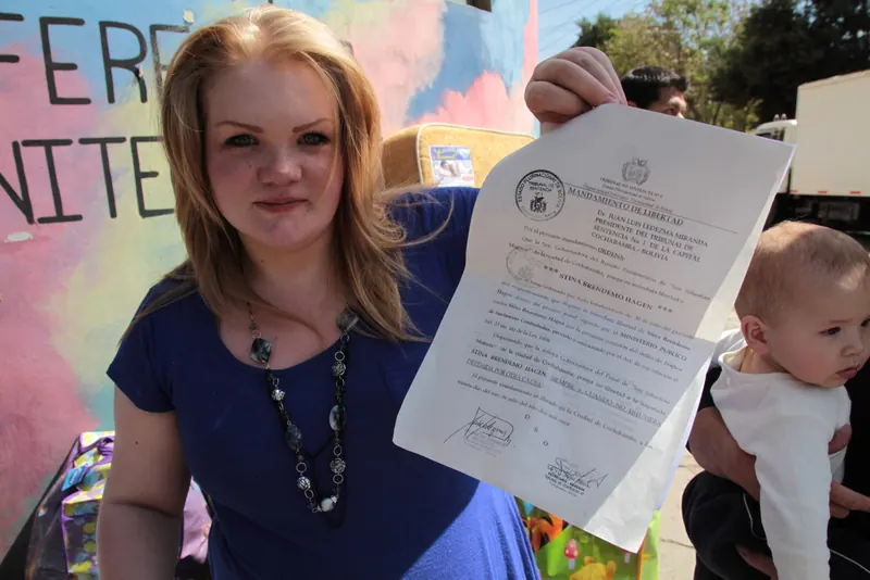 Una mujer muestra un documento oficial a la cámara. A su lado hay un bebé.