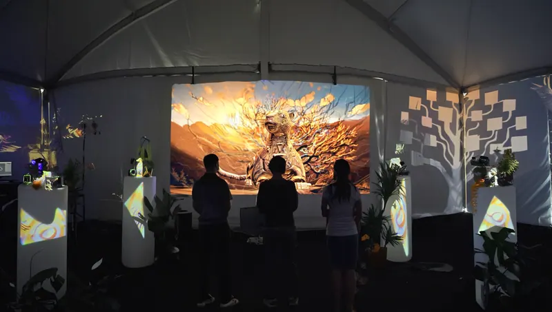 Tres visitantes frente a una pantalla que muestra un jaguar dorado, dentro de una carpa blanca con pedestales iluminados.