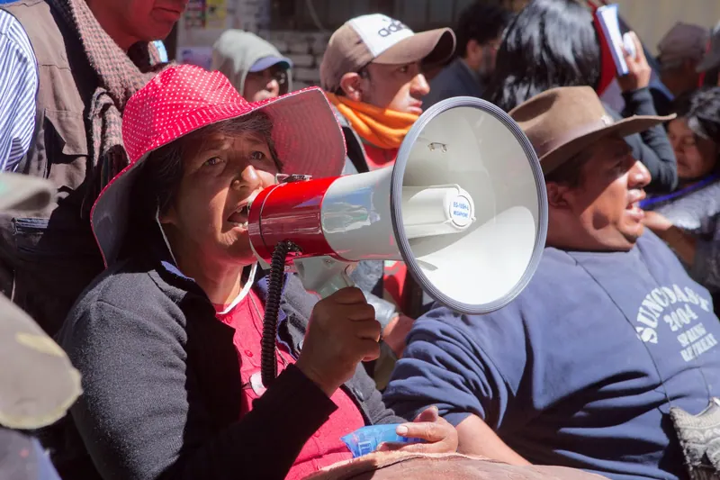 Una mujer con sombrero rosado habla por un megáfono.
