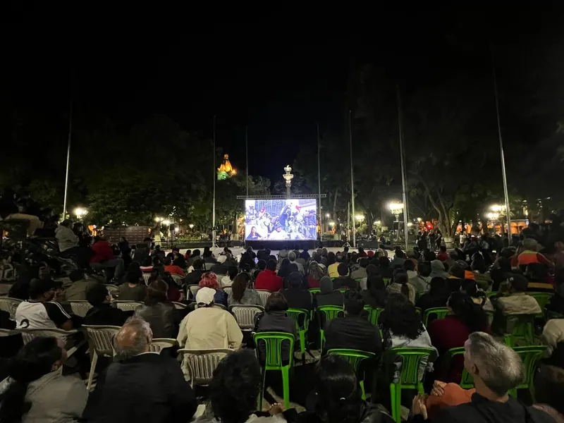 Una plaza llena mira una película en una pantalla al aire libre, de noche. El estreno de La Lucha en Bolivia, en una plaza principal, 2024.