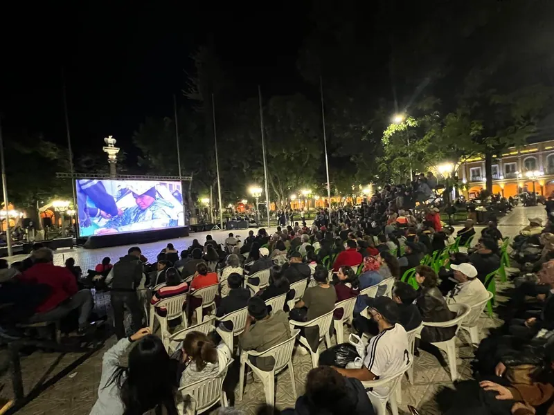 Una multitud mira una pantalla al aire libre en una plaza, de noche.