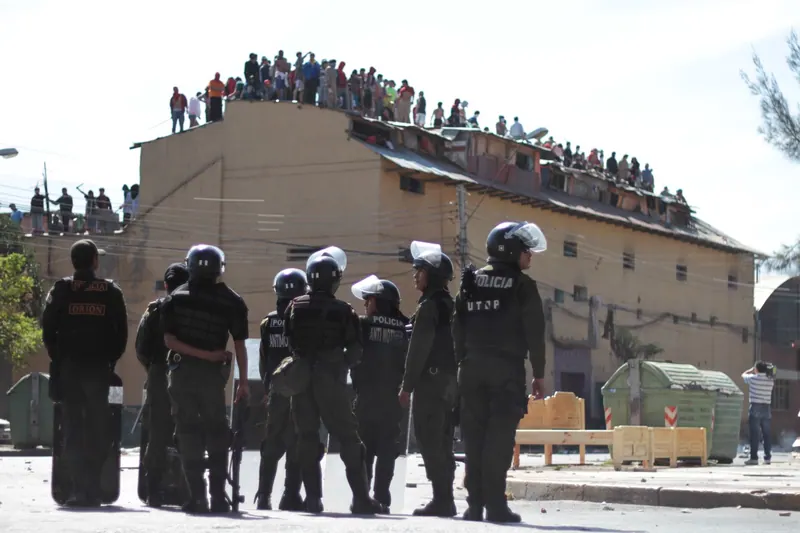 Policías antimotines frente a una cárcel. Los internos miran desde el techo. Cárcel de San Sebastián, Cochabamba.