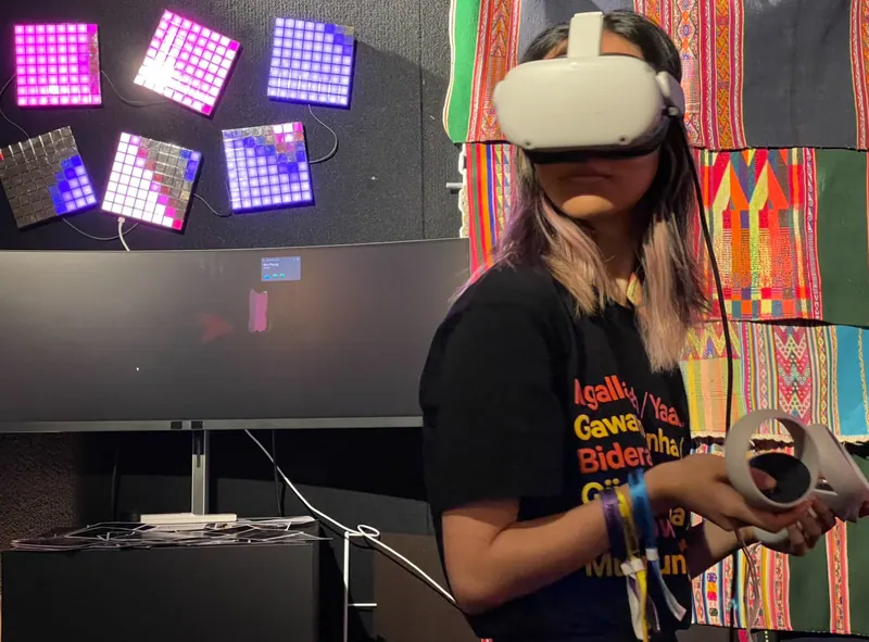 Una persona con visor de VR sostiene dos controles frente a unos tejidos.