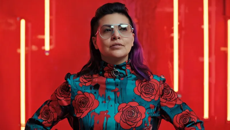 Retrato de una mujer con camisa de rosas frente a un neón rojo.