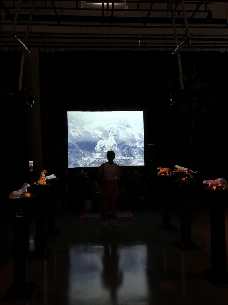 Una sala oscura con una pantalla encendida. A cada lado hay pequeñas figuras de animales que brillan.