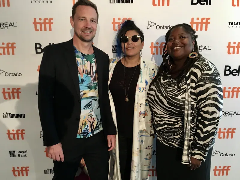 Tres personas posan frente a un fondo del TIFF. Festival Internacional de Cine de Toronto.