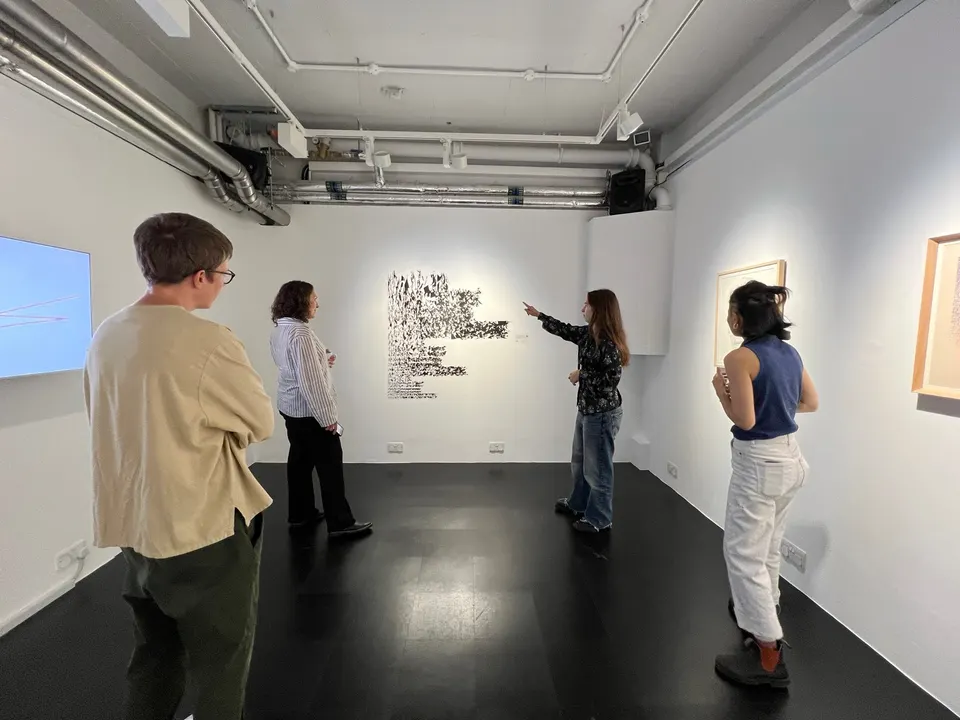 Cuatro personas están de pie en una galería blanca. Una de ellas señala una obra en la pared.