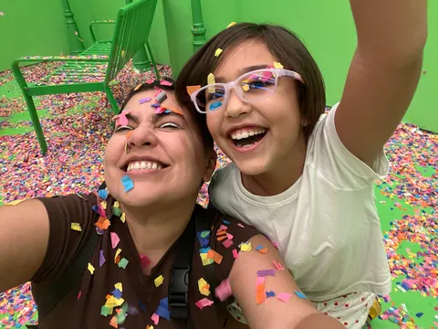 Una mujer y una niña se toman una selfie cubiertas de mixtura, delante de una pared verde.