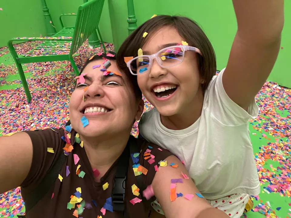 Una mujer y una niña se toman una selfie cubiertas de mixtura, delante de una pared verde.