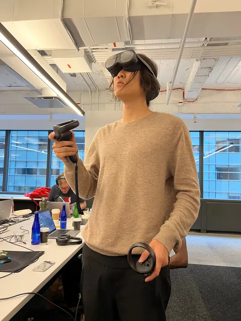 Una persona con un visor de realidad virtual sostiene un control en cada mano, en la oficina.