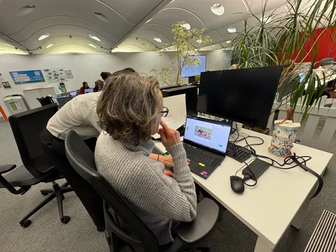 Una persona trabaja en una laptop en una oficina abierta con plantas.