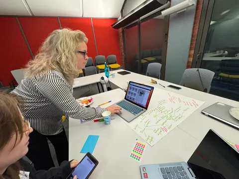 Una persona se inclina sobre una mesa con una laptop y un pliego grande de notas escritas a mano.