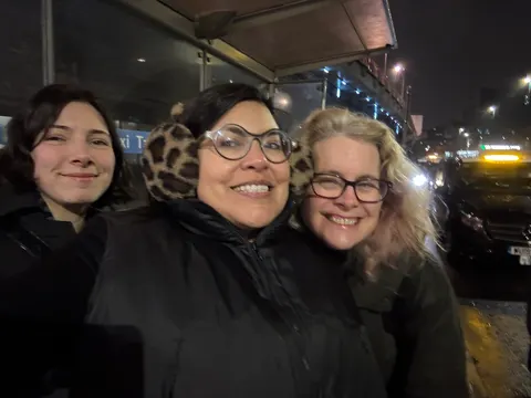 Tres personas sonríen cerca de la cámara, en la calle de noche.