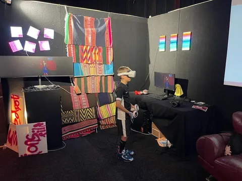 Un niño con un visor de realidad virtual está de pie en el stand de Prison X, entre aguayos, paneles de luces de colores y pantallas.
