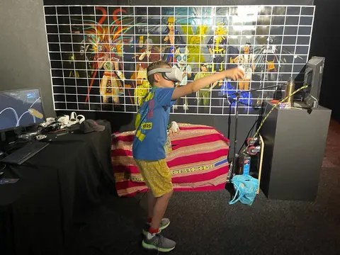 Un niño con un visor de realidad virtual estira un brazo, delante de una pared con imágenes de los personajes de Prison X.