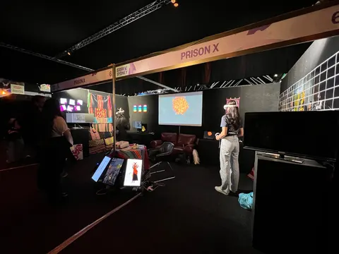 El stand de Prison X en SXSW Sydney: un letrero con el título, pantallas, aguayos y una visitante con un visor de realidad virtual.