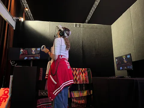Una visitante de chamarra roja lleva un visor de realidad virtual y mira hacia arriba, entre dos pantallas.