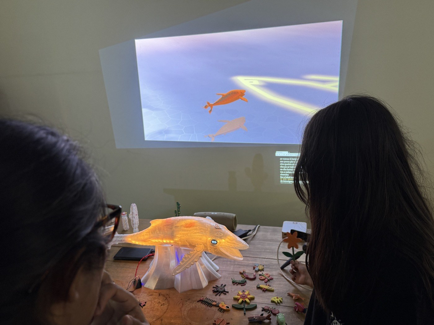 Dos visitantes la miran en el salar mientras la ballena impresa brilla naranja con ella